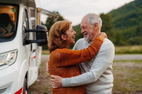 Happy senior couple embracing beside camper during RV vacation.