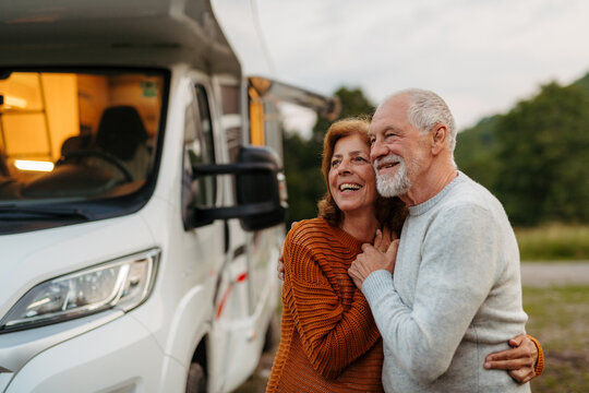 Senior couple standing and hugging outdoors at dusk, caravan holiday trip.