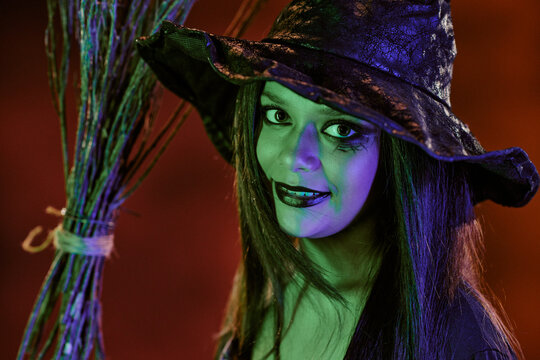 Portrait of Caucasian teenager girl wearing witch costume and holding broom during Halloween celebration. Image suitable for seasonal marketing campaigns and festive event promotions, close up