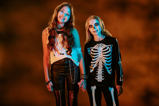 Portrait of diverse teenagers wearing Halloween costumes and holding hands while smiling. Image suitable for seasonal marketing campaigns and holiday event promotions, medium shot