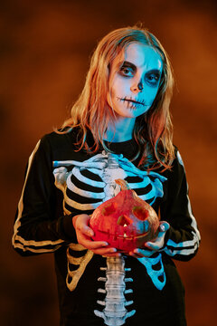 Portrait of Caucasian teenager wearing skeleton costume and makeup holding carved pumpkin. Image ideal for seasonal marketing campaigns and holiday promotions, vertical