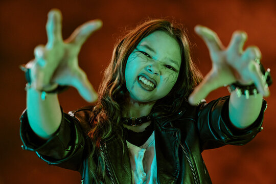 Portrait of Asian child girl wearing spooky Halloween makeup gesturing with hands towards camera. Image suitable for autumn holiday marketing campaigns and festive event promotions