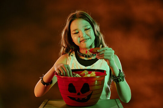 Asian child girl wearing Halloween makeup looking at candy bucket, celebrating autumn holiday. Image suitable for seasonal marketing campaigns and festive retail promotions