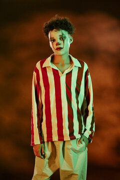 Portrait of African American teenager wearing clown makeup and striped shirt celebrating Halloween. Image is suitable for seasonal marketing campaigns and spooky event promotions, vertical