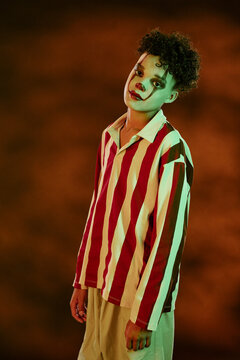 Portrait of teenager wearing spooky clown makeup for Halloween celebration. Image is suitable for seasonal marketing campaigns and festive event promotions, vertical