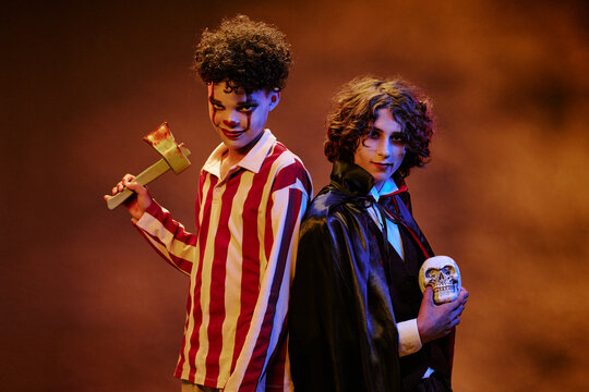 Portrait of diverse teenagers wearing Halloween costumes and holding spooky props while standing back to back. Image suitable for seasonal marketing campaigns and event promotions