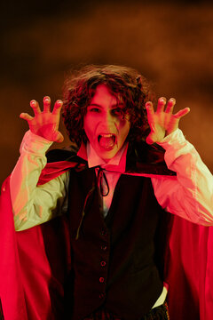 Portrait of Caucasian teenager wearing vampire costume gesturing claws and screaming during Halloween celebration, perfect for seasonal marketing campaigns, vertical