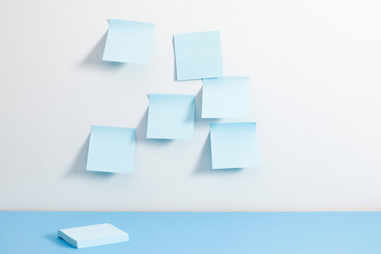 Blank Blue Sticky Notes on a White Wall Above a Blue Desk Surface. Minimalist Office Background for Reminders, Tasks, and Planning with Copy Space for Text. Business and Education Template.