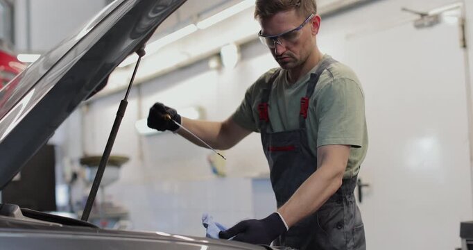Auto mechanic checking engine oil. Mechanic checking oil level in a car workshop.