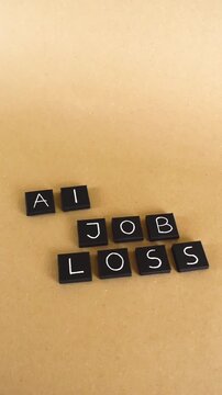 Floating camera shot of black tiles with white letters spelling AI Job Loss on a brown cardboard background, symbolizing unemployment and the impact of artificial intelligence on the economy