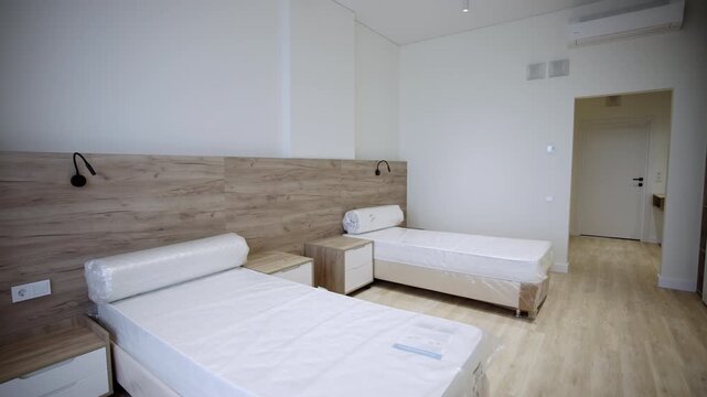 Modern double bedroom features twin beds with white sheets. Wooden headboard panels stretch across wall, holding small black lamps