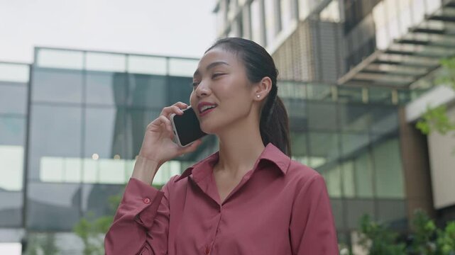 Successful asian business woman using phone outdoors.Happy businesswoman holding cellphone using smartphone or mobile phone standing or walking on city urban street,5g communicating with a colleague.
