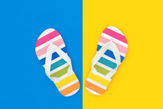 Rainbow flip flops fun summer casual footwear on contrasting yellow blue background. Colorful holiday multi colored spectrum thongs. Greeting card.