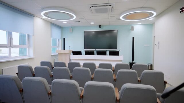 Conference hall includes rows of gray chairs television screen. Well-organized speaking positions equipped for professional presentations