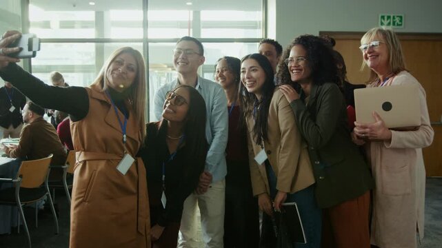 A group of happy business professionals take a joyful selfie at a conference event. They are smiling and laughing, enjoying their time together at the gathering, fostering positive connections.