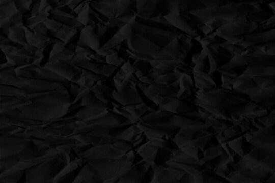 Dark black crumpled paper texture with subtle shadows and creases, abstract monochrome surface background