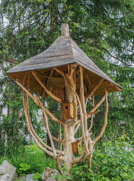 Rustic Wooden Birdhouse Pavilion Built Into Tree With Shingled Roof in Garden Setting