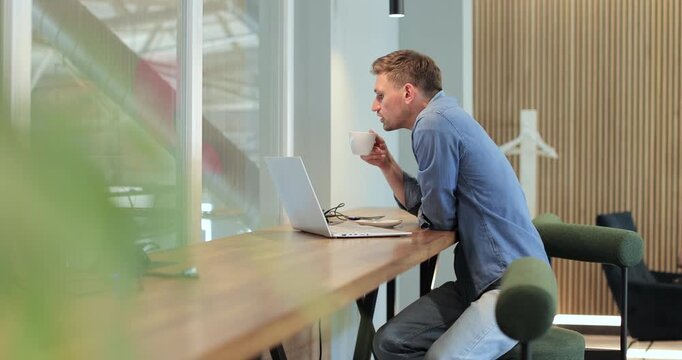 Young man waiting for car at car repair shop. Man working and drinking coffee while his car is being repaired. Automotive industry, auto care, service.