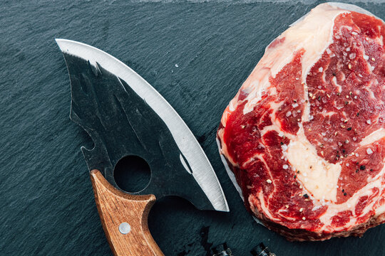 Fresh cut steak with a unique knife on a dark stone surface