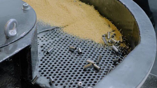 Vibratory finishing round bowl machine uses abrasive particles for polishing and cleaning metal details - close up view. Metalworking, industrial, equipment and manufacturing concept