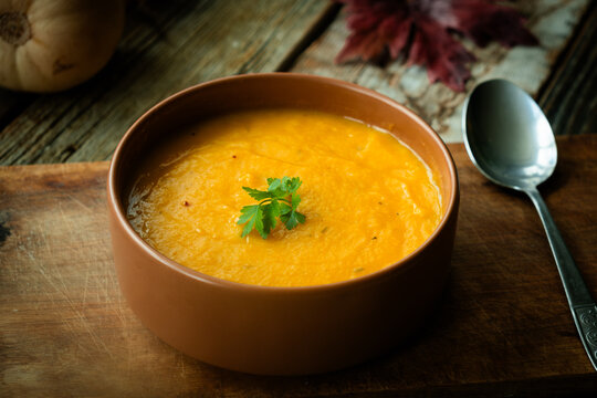 Pumpkin puree soup adorned with a parsley. Seasonal autumn meal, vegetable cream soup. Thanksgiving dinner in rustic style