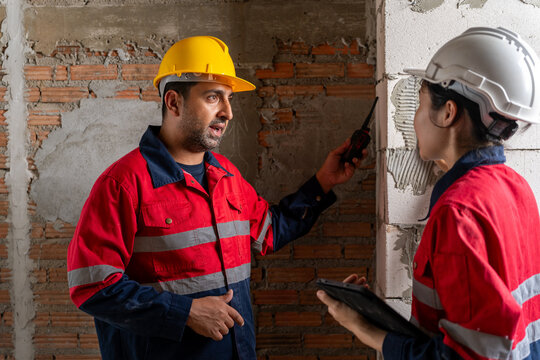 Engineers pointing and explaining construction plans together while looking at tablet at building site wall.
