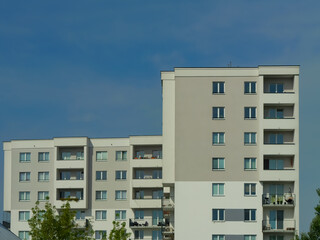 Fototapeta premium Modern white apartment building with balconies and geometric facade under a clear blue sky, representing contemporary urban housing, real estate and residential development