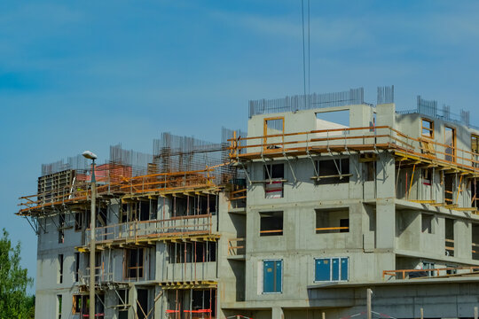 Multistory apartment building under construction with exposed concrete walls, steel reinforcement, formwork and safety railings against a clear blue sky