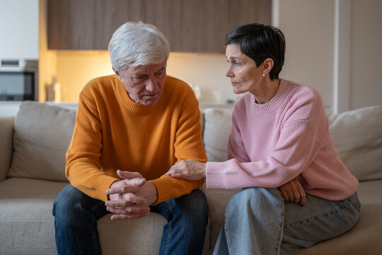 Concerned attentive elderly wife supporting emotionally stressed husband sitting on sofa at home, senior couple life challenges, loving woman shows understanding, empathy and family love, compassion.