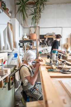 Focused man restorer attentively checking wooden door surface at workplace in restoration workshop, creative working process of antique furniture renovation in small business woodworking studio.