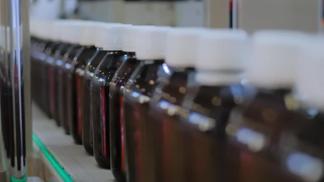 Close up view: moving empty amber glass bottles on conveyor belt at plastic packaging exhibition or factory. Production line, demonstration mode of bottle shrink sleeve labeling machine
