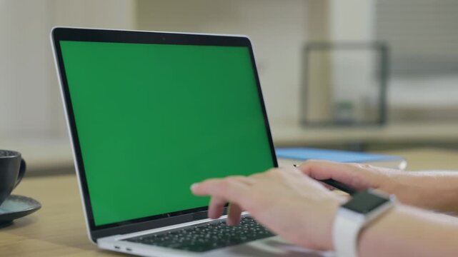 Woman Working On Laptop Computer with Green Mock Up Screen At Home Office Space. Female Freelancer Browsing Green Laptop Screen Writing Information in Notebook
