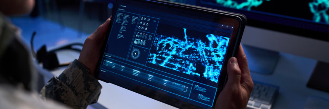 Caucasian soldier holding tablet with digital map interface, analyzing tactical data. Image represents military technology and cyber defense, suitable for defense industry marketing