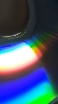 Bright rainbow light reflection on a compact disc surface with central hole. background, texture, abstract neon glow, closeup view, colorful prism refraction.