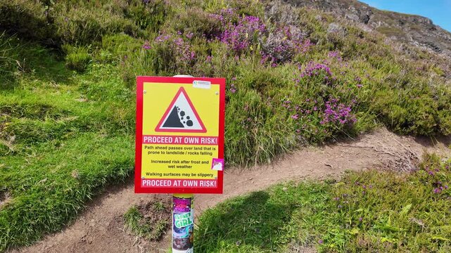 a warning sign at the start of a rough hiking trail on Quiraing mountain in Isle of Skye, Scotland on a sunny, summer day