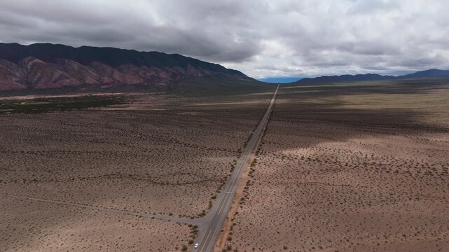 Straight Recta del Tin Tin highway crossing vast desert plain, aerial panoramic overview with large cloud shadows crossing road, symmetrical ending