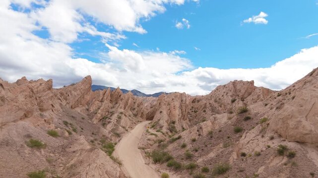 Winding desert road through Quebrada de las Flechas beneath blue sky and clouds, aerial descend dolly to empty pathway