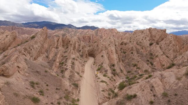 Drone symmetrical pullback above straight dirt road in Quebrada de las Flechas sandstone canyon, aerial, Salta Region Argentina