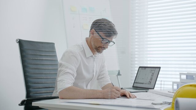 Engineer drawing blueprints while working on laptop in modern office, planning construction projects, architectural design, industry development and innovative building solutions