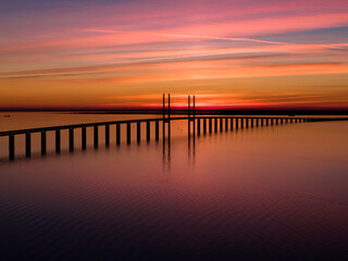 Fototapeta premium Scenic view of the Öresund Bridge connecting Sweden and Denmark, photographed from the Malmö side during a vivid colorful sunset over the Öresund Strait.