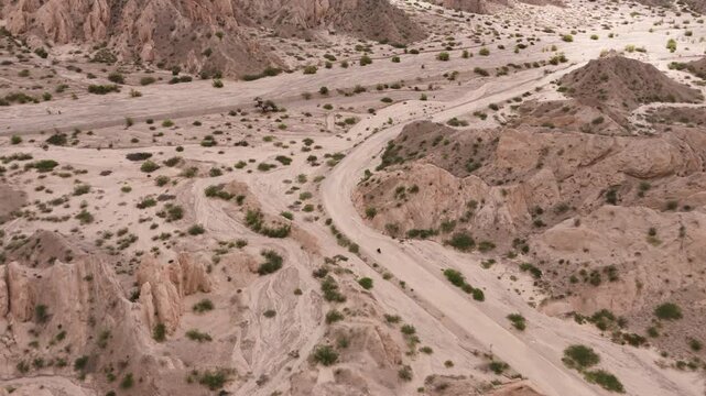 Motorbike riding through Quebrada de las Flechas desert road between rugged rock formations, aerial tracking follow, Salta Region Argentina