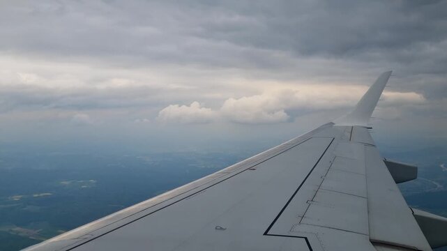 Passenger window view from an airplane flying through a sea of clouds under a dark sky, with the wing visible, capturing the beauty of air travel, transportation and tourism