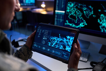Caucasian male soldier holding tablet with digital map in high tech control room, analyzing tactical data. Image suitable for defense technology and cybersecurity marketing, close up shot