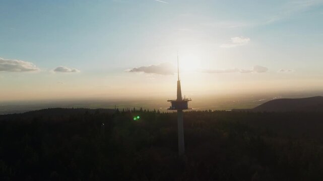 The Melibokus tower is silhouetted against a glowing sunset over hazy hills