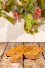 Obraz premium Vertical wooden product podium on rustic table with blurred grapevine background for autumn harvest mockup