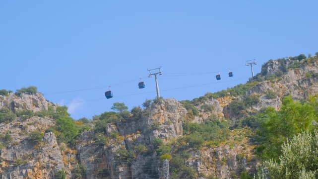 Ropeway and cable car cabins moving against blue sky over Mount Babadag in Mugla, Turkey. Aerial rope transit, gondola lift - view from the foothills. Sightseeing, and public transportation concept
