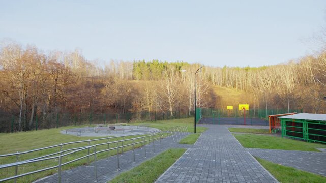 Paved stone walkway curves towards outdoor basketball court. Recreational park area features clean pathways and cozy wooden gazebos