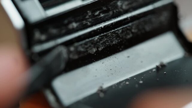 Macro shot with shallow depth of field: a tool scrapes crumbled old light seals from a vintage 35mm camera, the sharp focus falling off into soft bokeh. Detailed restoration of analog gear before rene