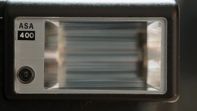 Close-up on an empty frame, then a flash for for an old analog cameras is held in, shown in tight detail, and taken back out. A clean insert shot of vintage analog gear.