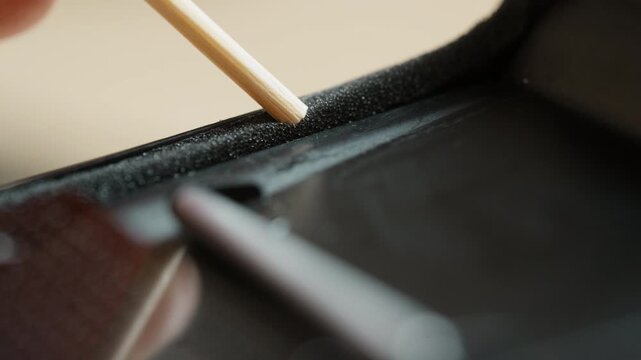 Close-up of fresh self-adhesive light seals in a vintage 35mm camera, pressed firmly into the film channel with a small wooden stick. The finishing step of analog restoration &ndash; seating the seals light